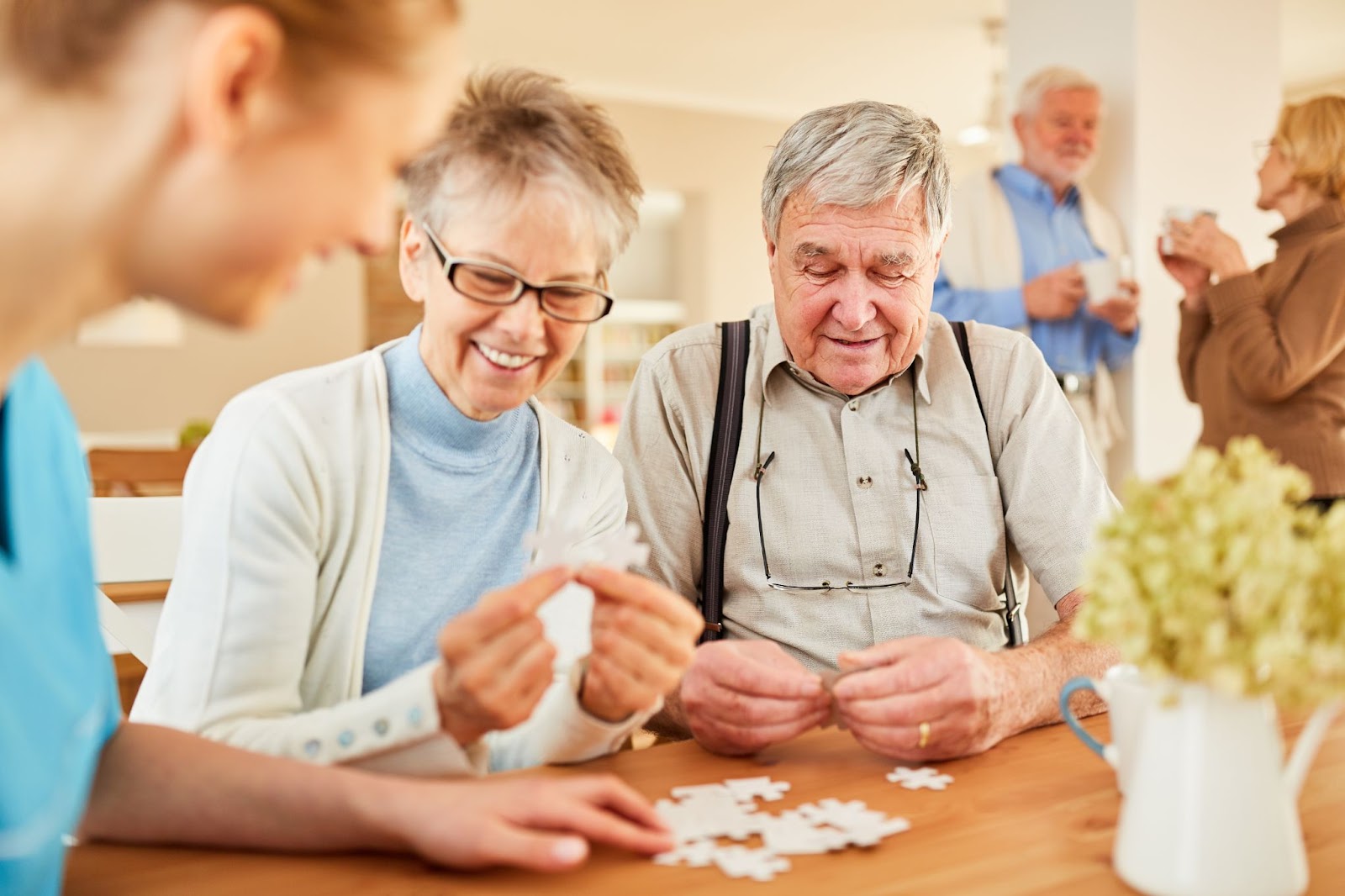 Two older adults smile while sitting and doing a puzzle with help from a staff member.