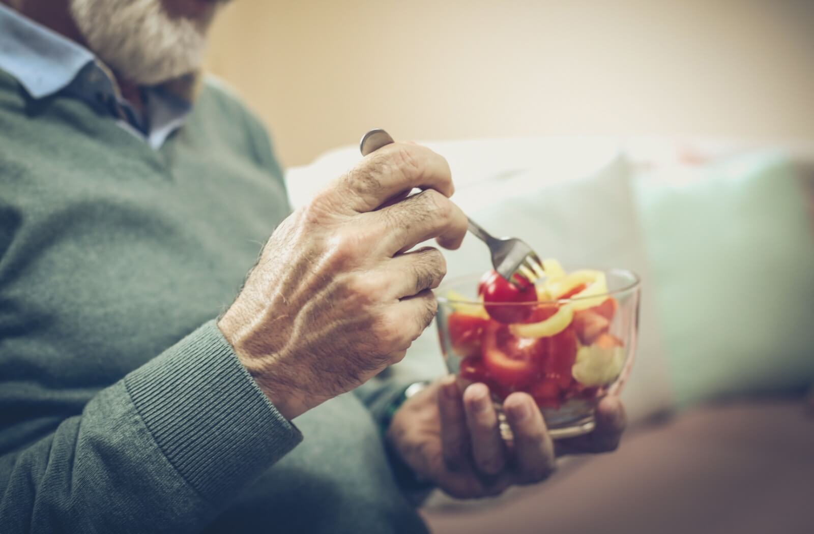 A close-up image of a senior enjoying a healthy snack of fresh vegetables cut up in a bowl.