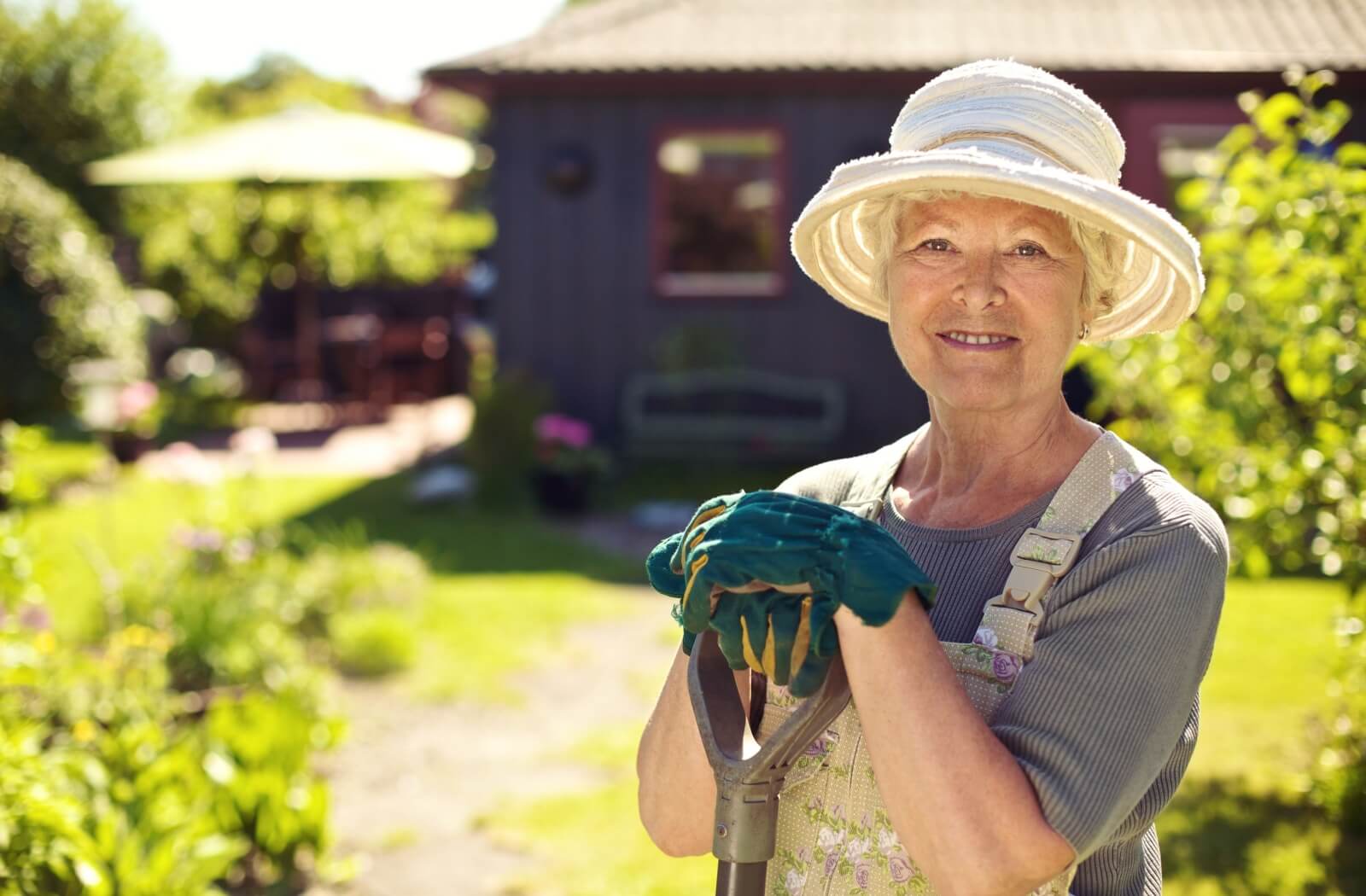 A smiling senior wearing a wide-brimmed sun hat while spending time outside tending to their garden.