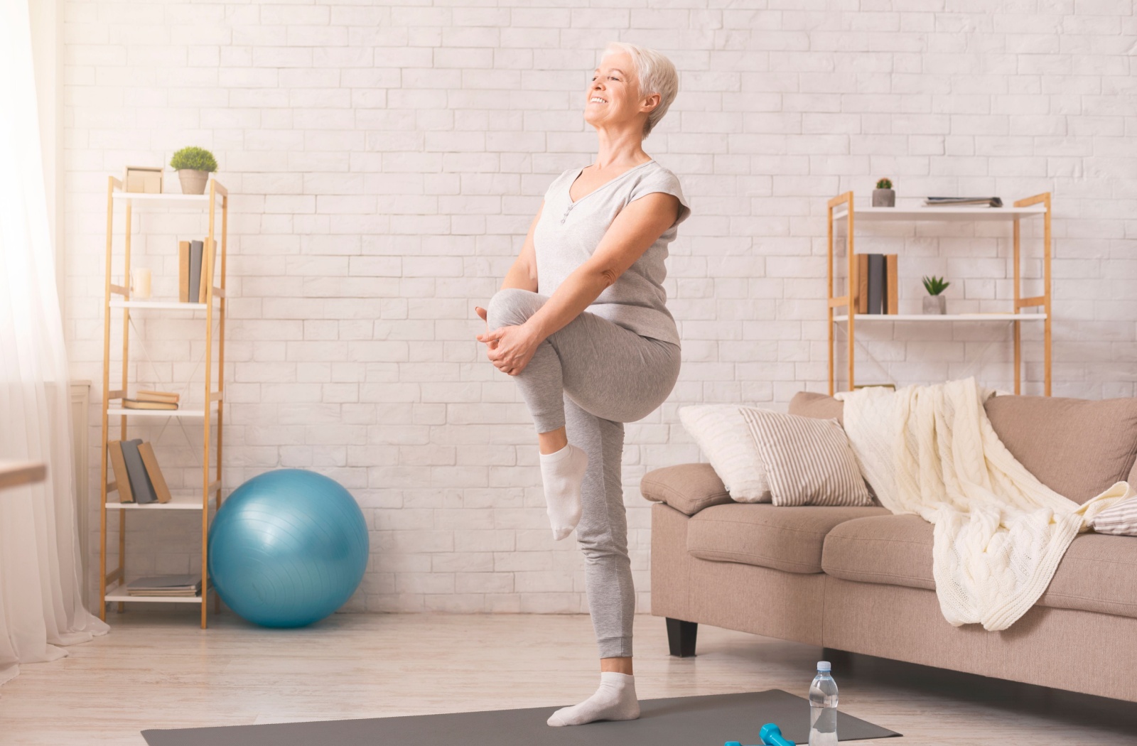 A senior balances on one leg in their living room to improve their balance.