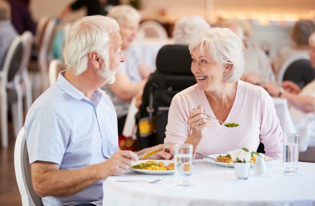 An older man and older woman sitting at a table smiling and eating a meal