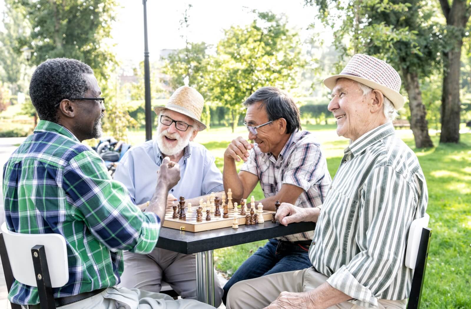 A group of happy seniors sit around a chess board outside, enjoying an afternoon of board games in the sun.