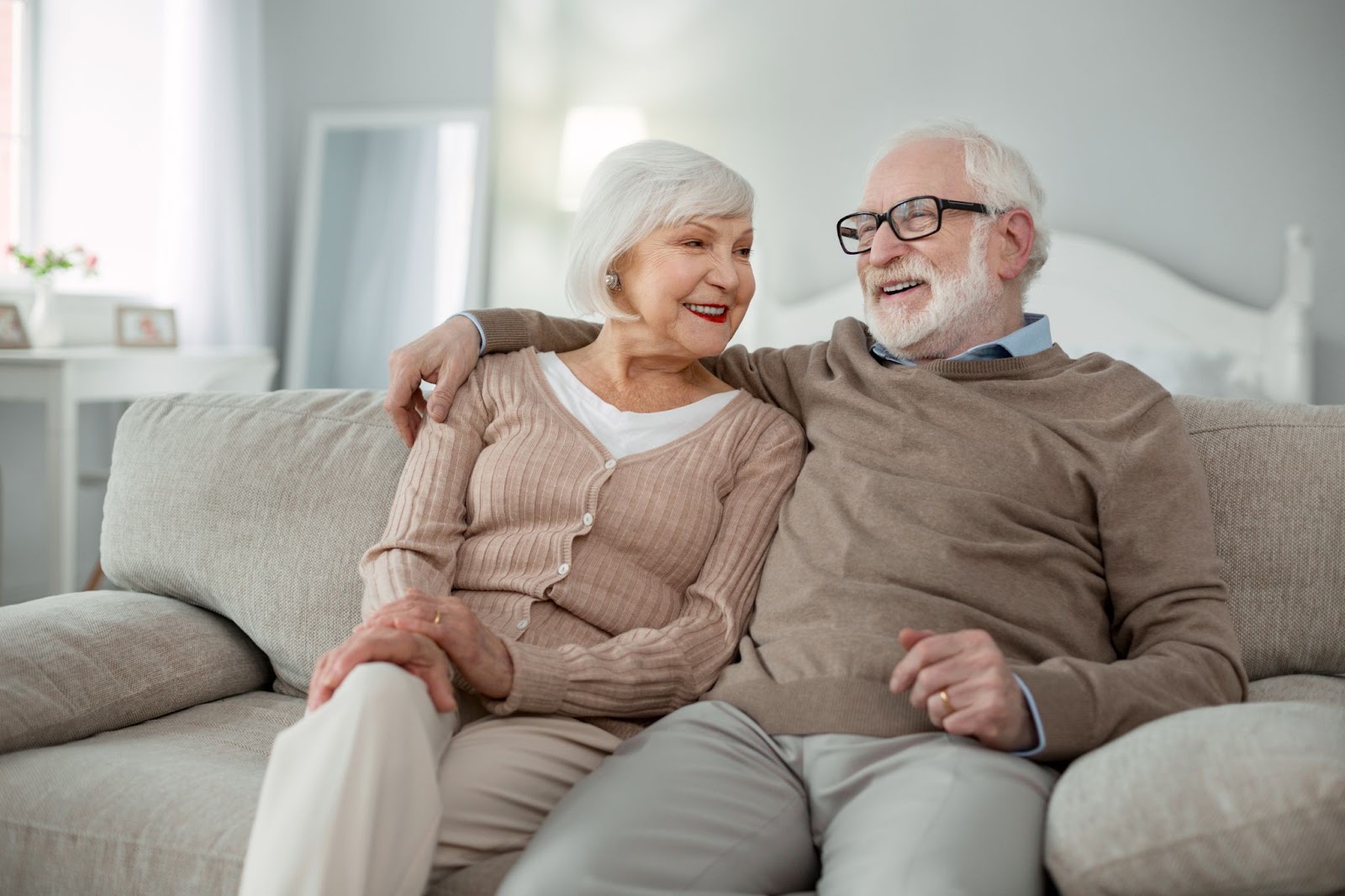 Smiling older adult sitting on the couch next to his happy wife with his arm around her shoulder.