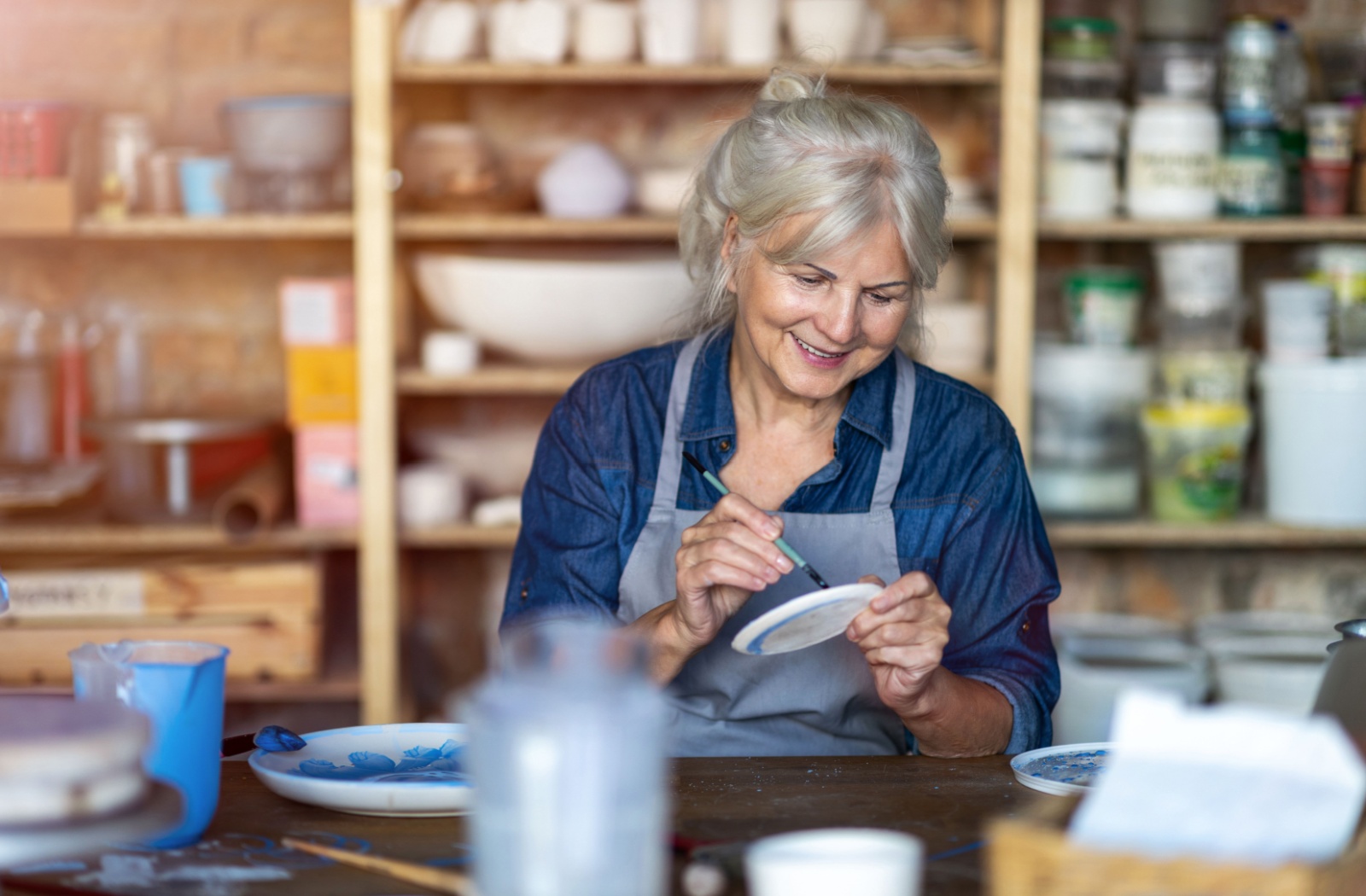 A senior smiles while painting pottery at a pottery studio in a senior living community.