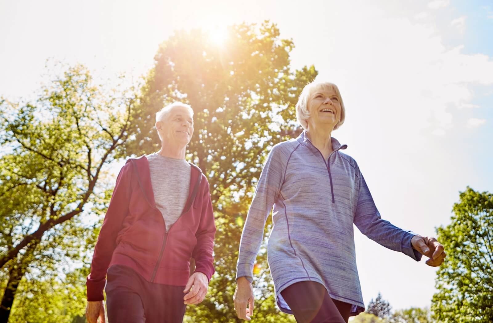 2 older adults smile while walking together through a beautiful park in the summer