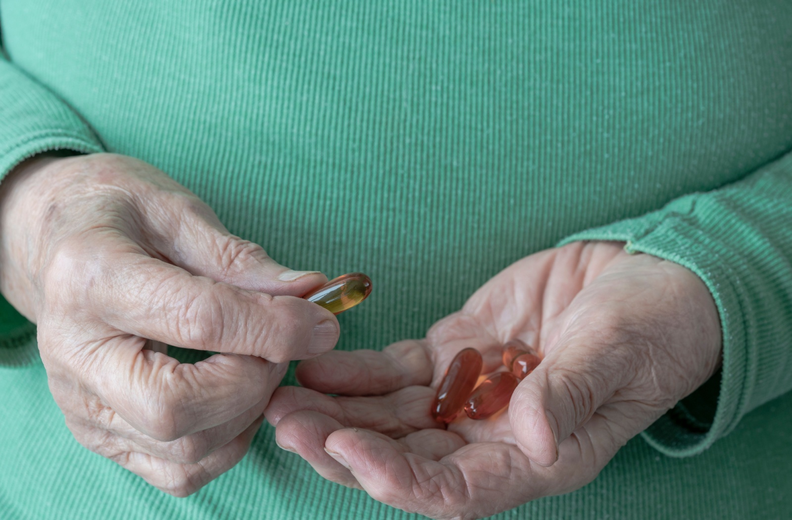 Close up of a senior resident in a teal sweater holding some Omega-3 vitamin pills.